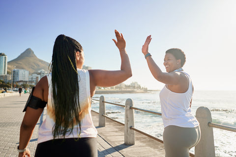 Women walking on promenade next to beach high-fiving each other