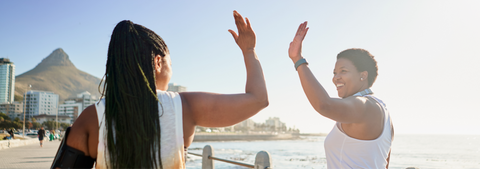 Women walking on promenade next to beach high-fiving each other